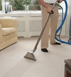 Professional carpet cleaner using a hot-water extraction wand and hose machine in a living room in Eugene, OR.