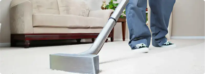 Carpet cleaning technician using a hot-water extraction wand on a light-colored carpet in a living room, Eugene, OR.