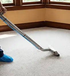 Steam carpet cleaning technician using a hot-water extraction wand on a residential carpet, wearing blue protective shoe covers Eugene, OR.