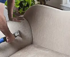 Professional upholstery cleaner deep-cleaning a fabric sofa with a handheld extraction tool and hose in Eugene, OR.